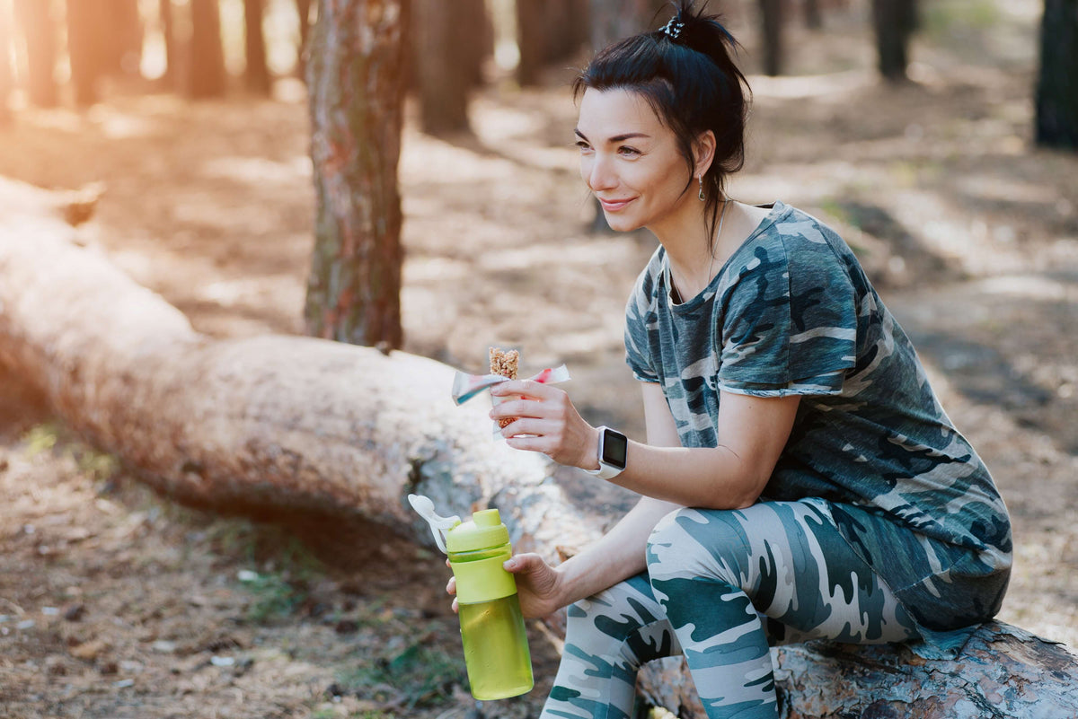 Frau nach dem Sport, mit Proteinriegel und Aminosäuren-Shake
