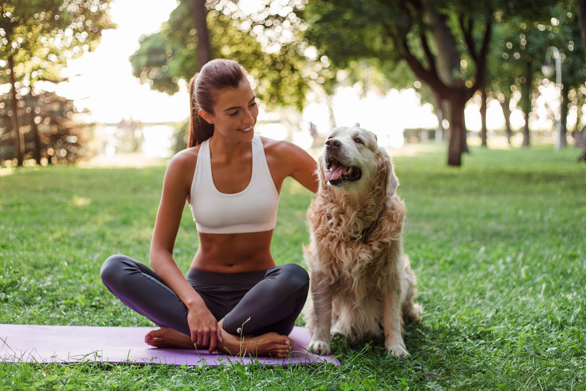 Cortisol senken - Frau reduziert Stress beim Yoga im Park mit Hund