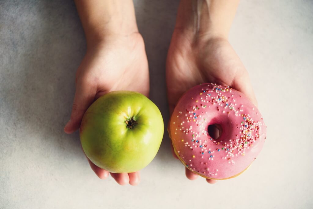 Hände bieten Apfel und Donut an - Ernährung beeinflusst Diabetes-Risiko