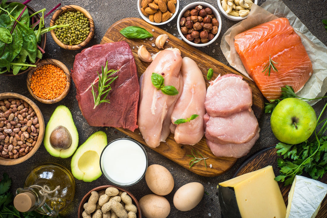 Fettreiche Speisen auf einem dunklen Tisch, unter anderem Fleisch, Fisch, Käse, Eier, Nüsse, Saaten, Avocado
