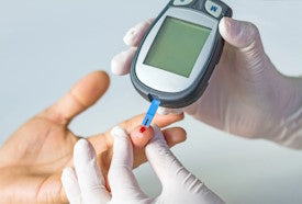 Finger wird mit Blutzucker-Messgerät gepikst
