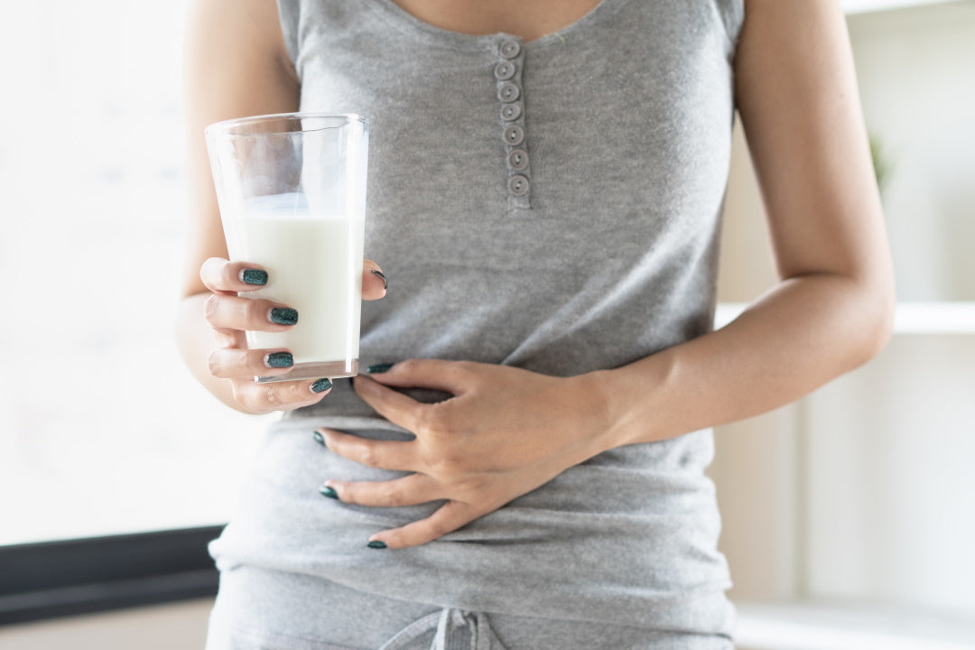 Frau hält in der rechten ein Glas Milch, mit der linken hält sie sich den Bauch
